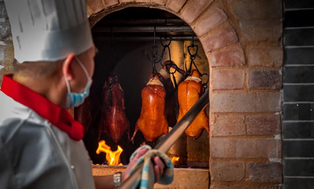Beijing chef roasting Peking Duck over fruitwood charcoal, preparing crispy-skinned and tender meat on local food trail