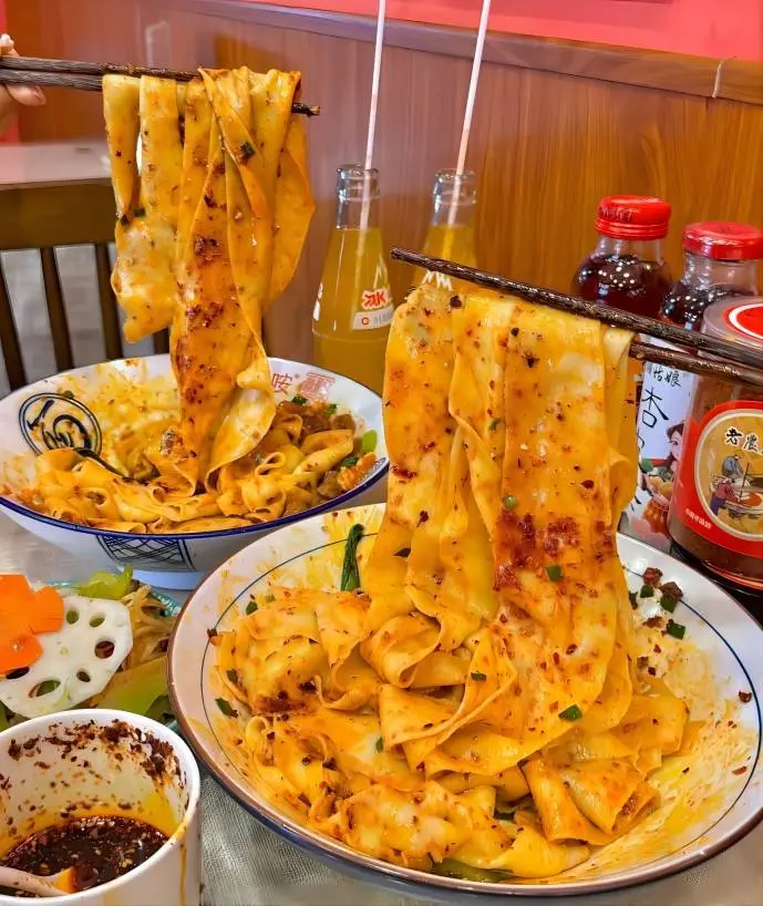 Biangbiang noodles Xi’an local food, tourist lifting wide noodles with chopsticks