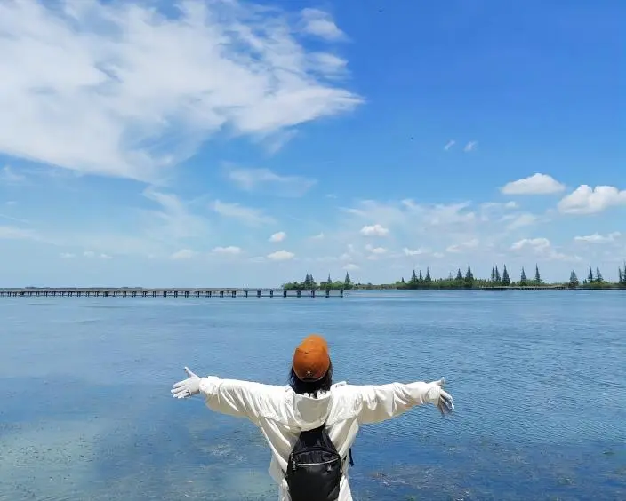 A tourist facing Dianshan Lake, Shanghai, with arms open, enjoying nature and embracing the scenic view from the lake shore.