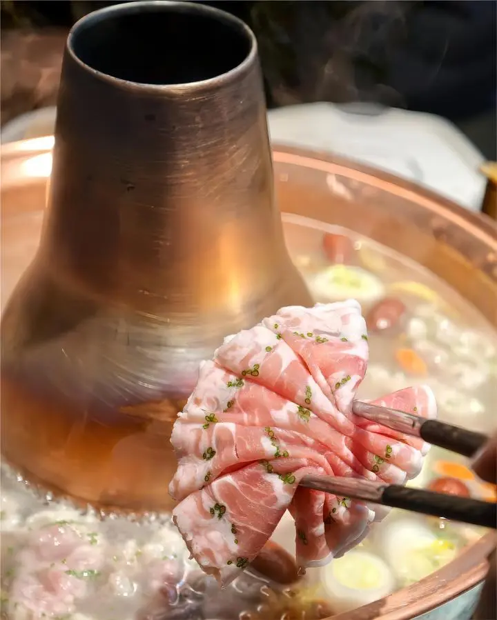 Close-up of tender mutton slices being cooked in a copper pot hot pot in Beijing
