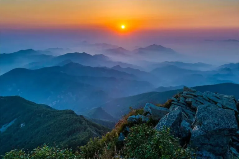 Sunrise over Wulingshan Mountain in Beijing, with golden light illuminating the peaks and forests.
