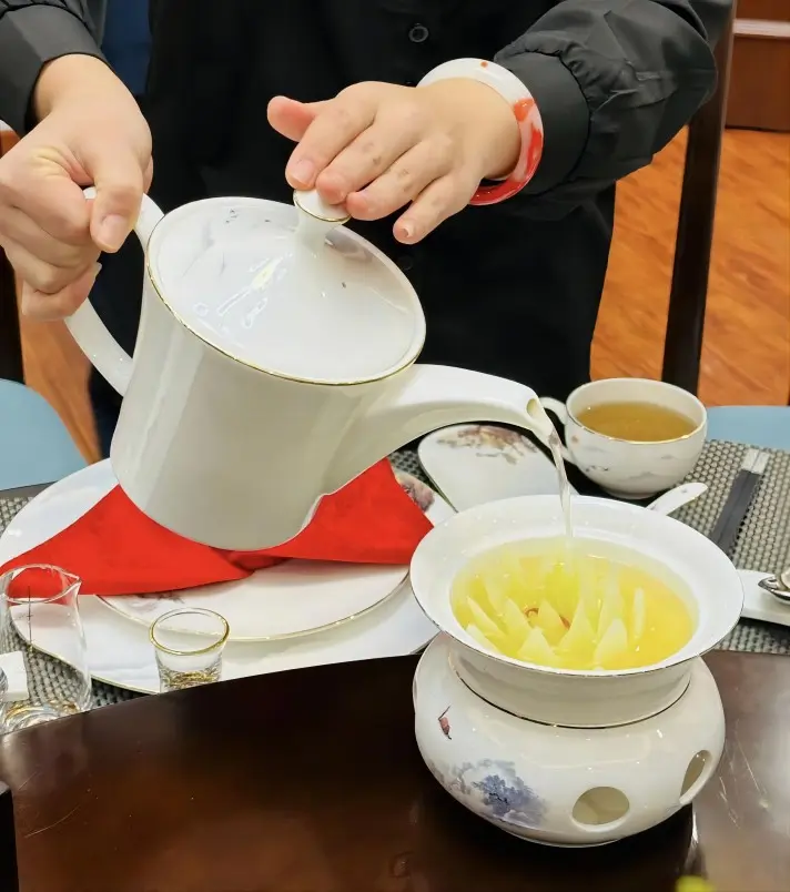 A server pouring clear broth into Kai Shui Bai Cai, a classic non-spicy dish in traditional Sichuan cuisine