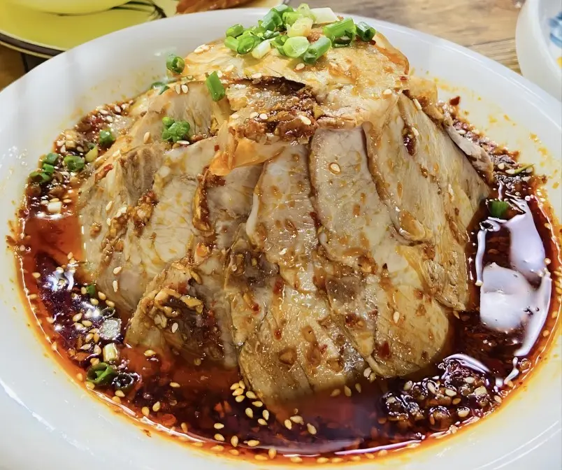 Close-up of Suan Ni Bai Rou (Garlic Pork) slices with rich garlic sauce, Chengdu Sichuan street food
