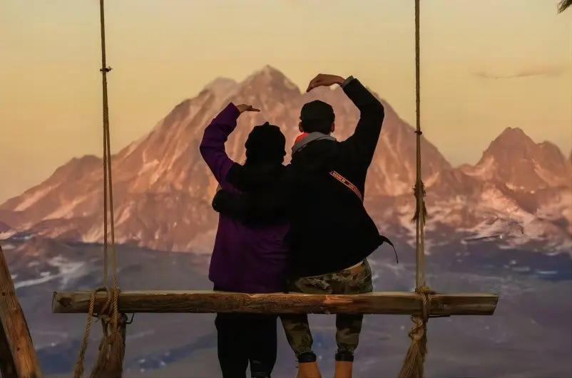 Visitor riding the cliff swing at YuZiXi with snow mountains and open sky behind
