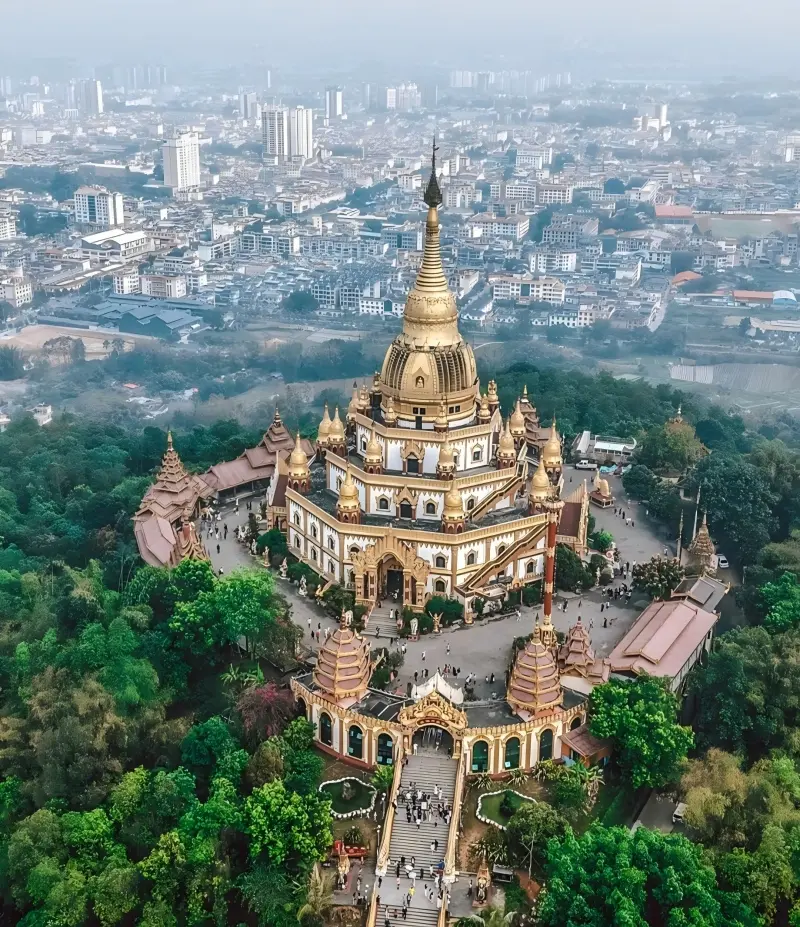 Aerial view of Menghuan Golden Pagoda in Mangshi surrounded by the city skyline.