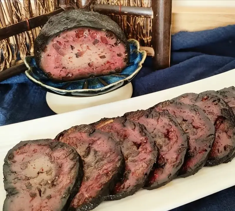 Close-up view of sliced Tujia blood tofu, a smoked local specialty made from soybean curd, pork, and pig blood.