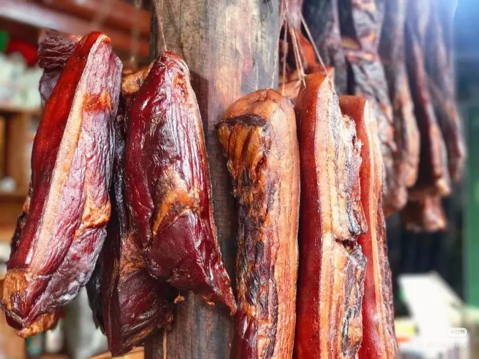 Close-up view of sliced Tujia smoked pork (cured bacon), showcasing its rich golden-brown fat and savory lean meat.
