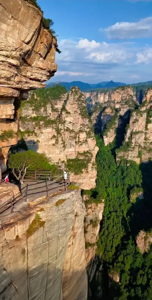 A traveler standing at the Air Corridor cliffside path with open arms, taking in the dramatic mountain views of Yangjiajie