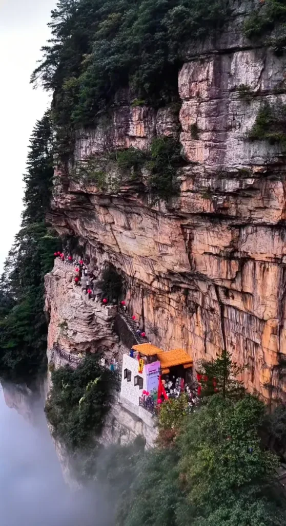 A distant panoramic view of Oulong Village perched dramatically on top of rugged cliffs in Yangjiajie, Zhangjiajie