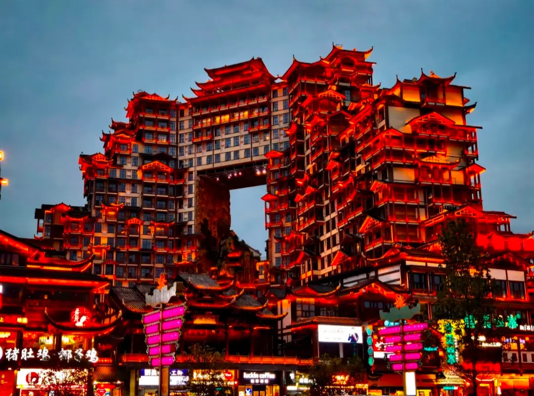 Illuminated view of the 72 Strange Towers (72 Qilou) landmark at night in Zhangjiajie, China, set against a backdrop of towering mountains.